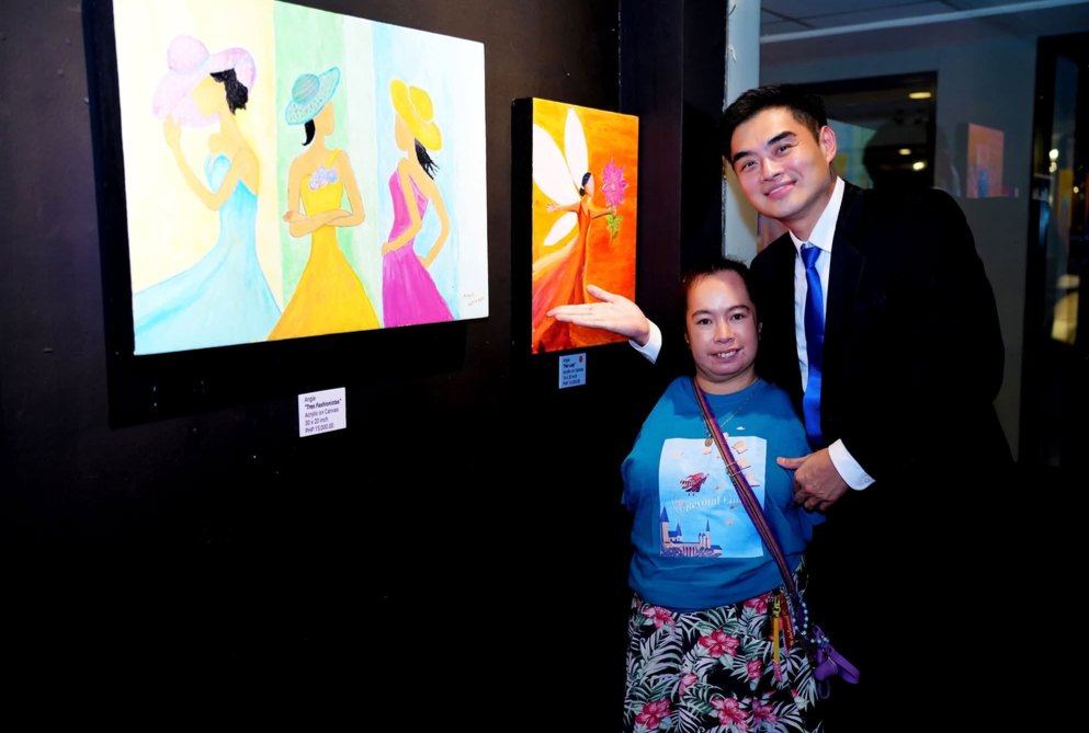 President Reginald Yu with Angie beside her vibrant paintings, "Tres Fashionistas" and "Fair Lady," at "Beyond Limits." A joy to celebrate the imagination and dedication she brings to every canvas, and to share this proud moment in her journey with the Angels of Rendu. Angie is a talented resident artist at Hospicio de San Jose who paints incredible works of art using her feet despite having no hands or arms.
