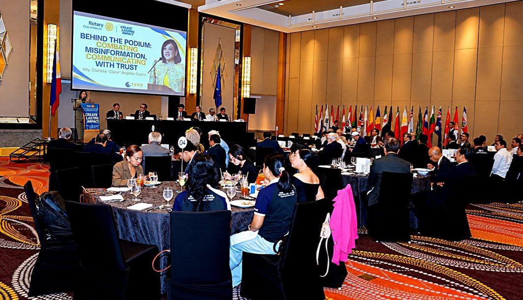 Across the ballroom, Rotarians and guests turn toward the podium as Atty. Claire addresses Rotary Manila's 14th Weekly Membership Meeting. Flags lining the room recall Rotary's international fellowship, while the afternoon's subject speaks to a concern shared across borders: communicating with trust amid misinformation. Around the luncheon tables, members hear an invitation to examine evidence, exercise discernment, and consider the consequences of every message they share. This wider view captures the setting in which fellowship and public dialogue meet, giving familiar Rotary principles fresh relevance in the everyday choices of a connected world.