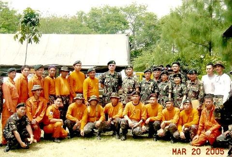 Maj. Gen. Alan Cabalquinto, Commander of the Army Special Forces (Airborne) Group, is positioned to the left of the principal subject. Standing fourth from the right is Capt. Sharon Reyes, while MSgt. Henry Hernia is seen kneeling fifth from the right. The photograph captures members of the elite Special Forces unit during a moment of camaraderie and professionalism.
